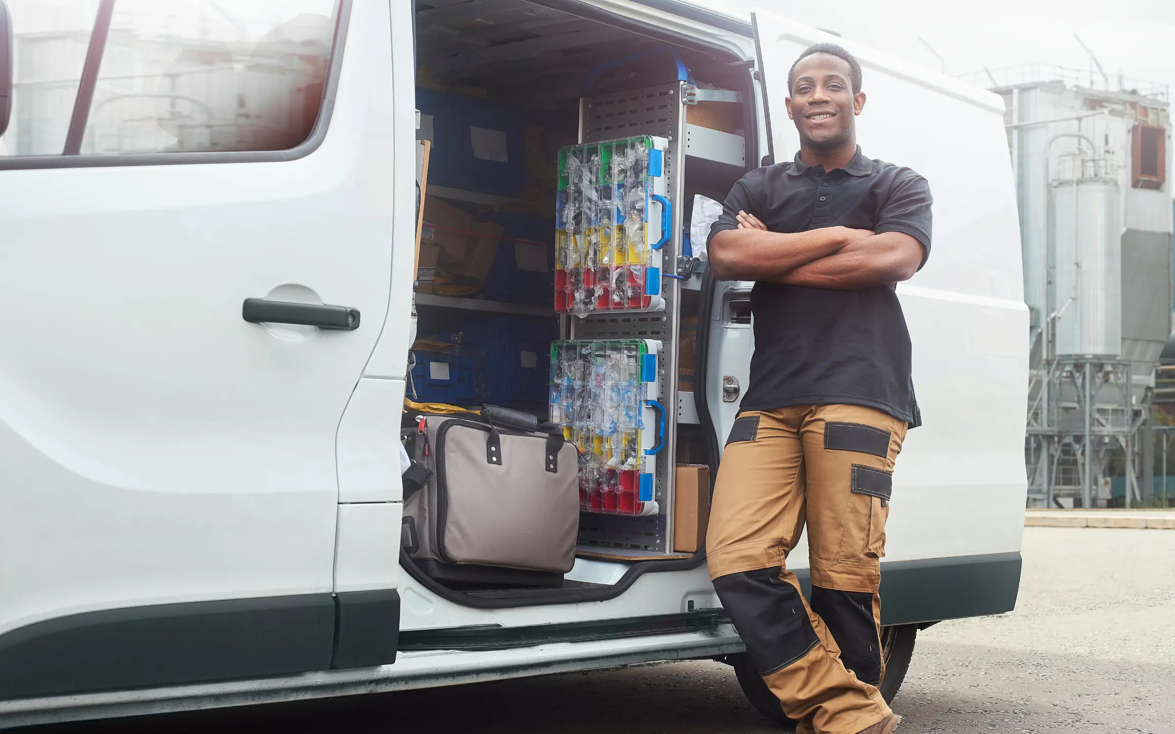 A tradesman standing beside an open service van stocked with parts and tools at a job site