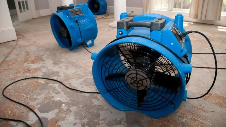 Commercial air movers drying the floor of an empty room during water restoration