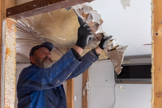 A worker pulling down damaged ceiling material during interior demolition