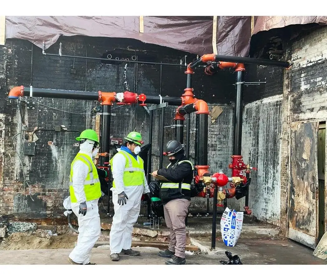 Inspectors in protective gear documenting a fire-damaged sprinkler riser system in a building