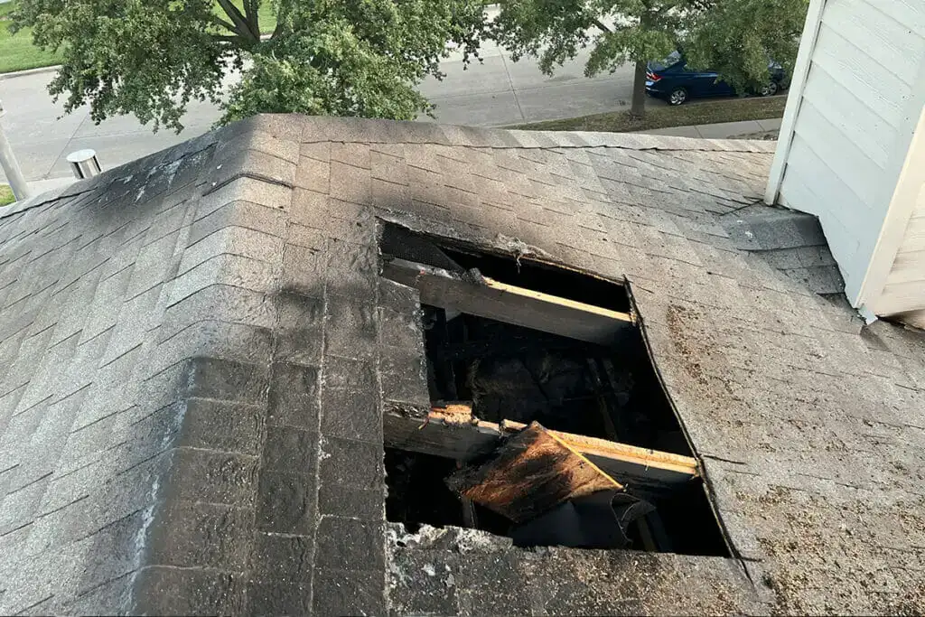 A close-up of a damaged roof section with a hole exposing charred and rotted decking — restoration and radon insurance in Colorado