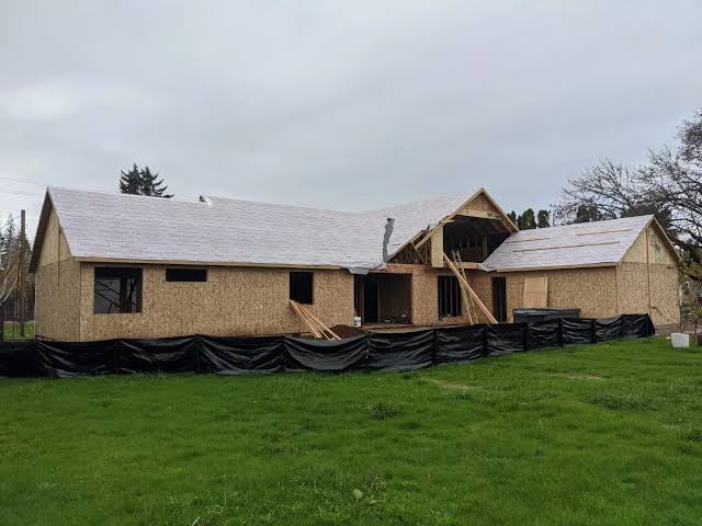 A house being rebuilt with new sheathing and roof decking behind a silt-fence perimeter — restoration and radon insurance in Texas