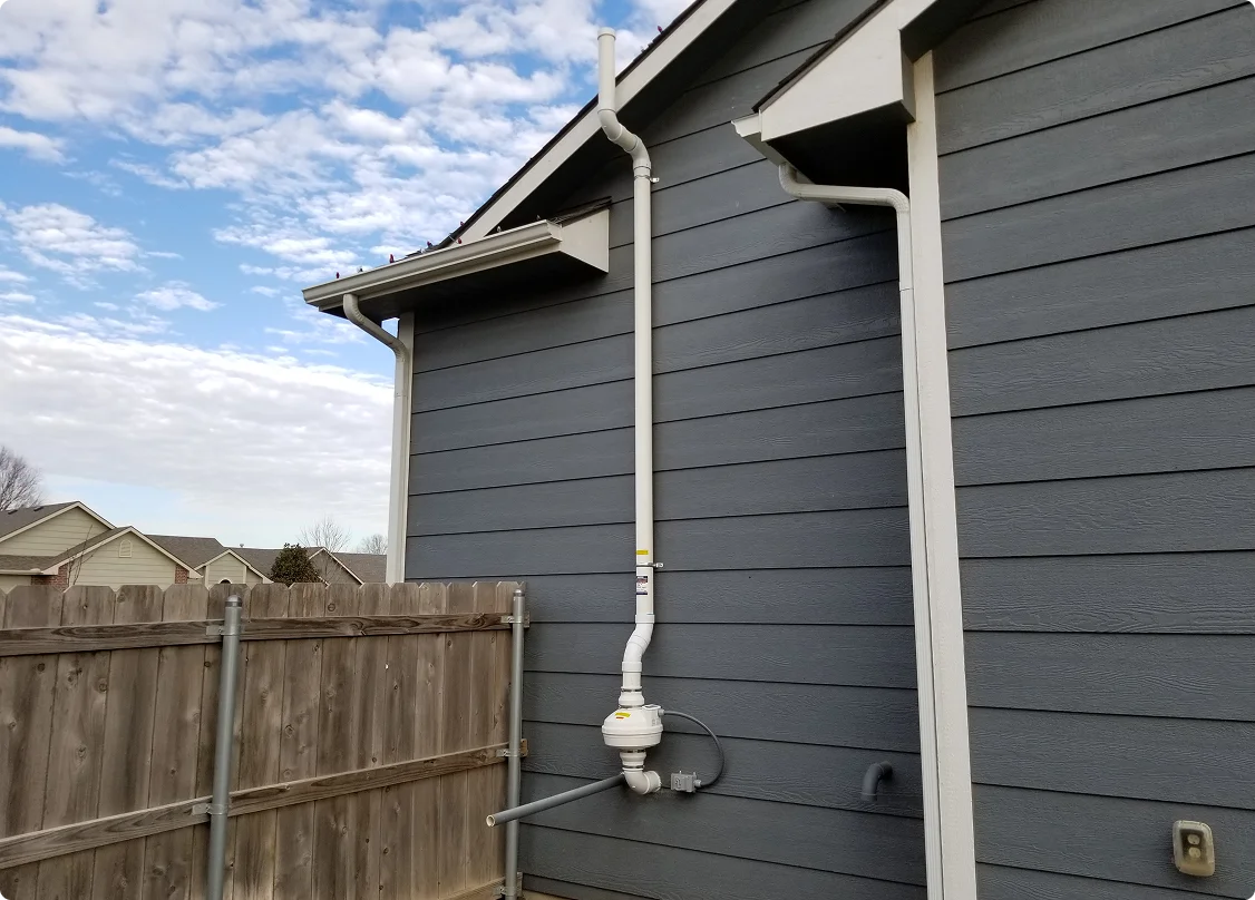 An exterior radon mitigation vent pipe and inline fan mounted on the side of a house — radon mitigation insurance in Delaware