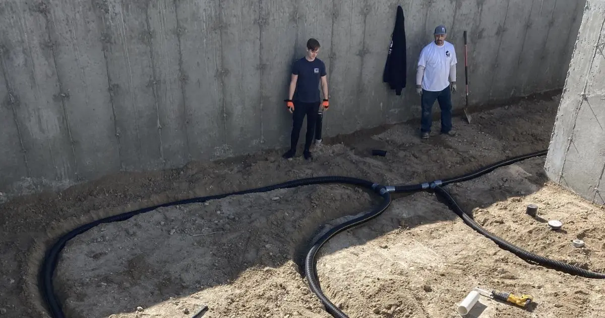 Two workers installing perforated sub-slab depressurization tubing in a new concrete foundation — radon mitigation insurance in California