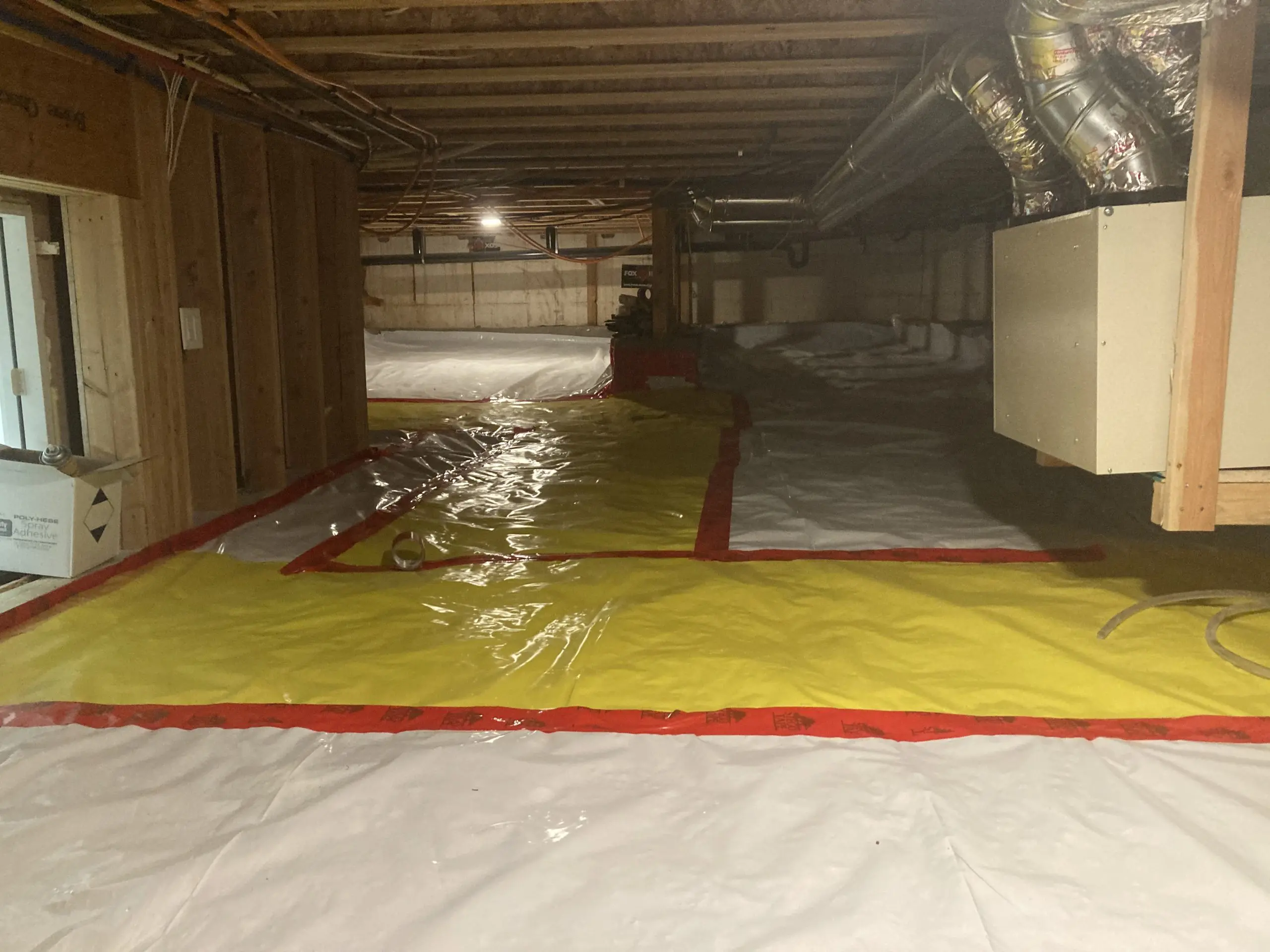 A crawlspace sealed with a reinforced vapor barrier and taped seams beneath a home’s ductwork — radon mitigation insurance in Georgia