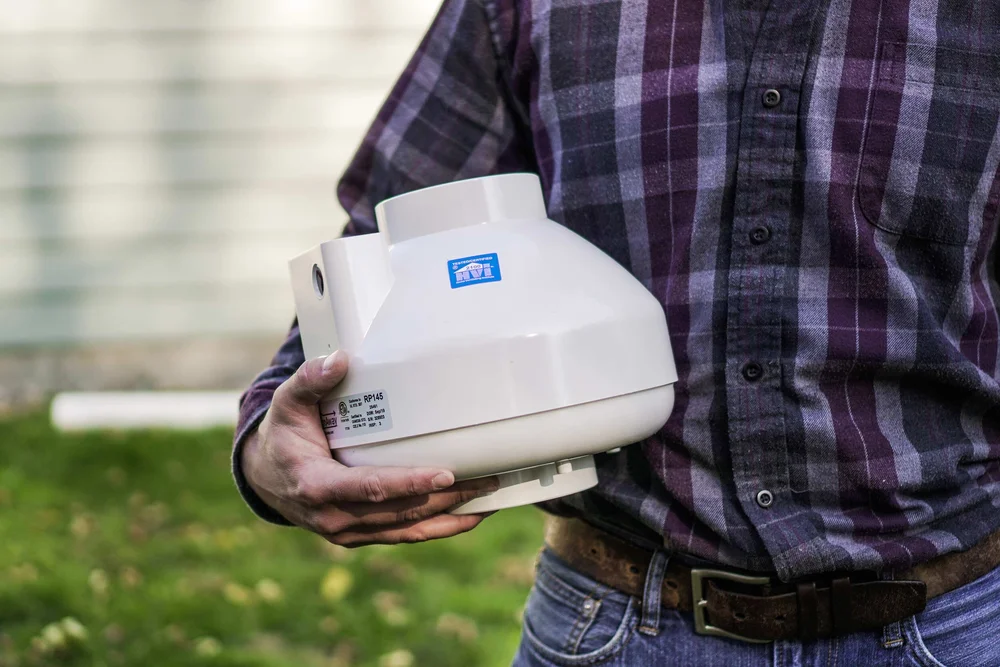 A contractor holding a radon mitigation fan unit outside a home — radon mitigation insurance in California