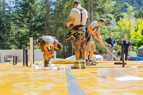 A crew applying a fluid-applied vapor membrane across a raised subfloor deck — radon mitigation insurance in Illinois