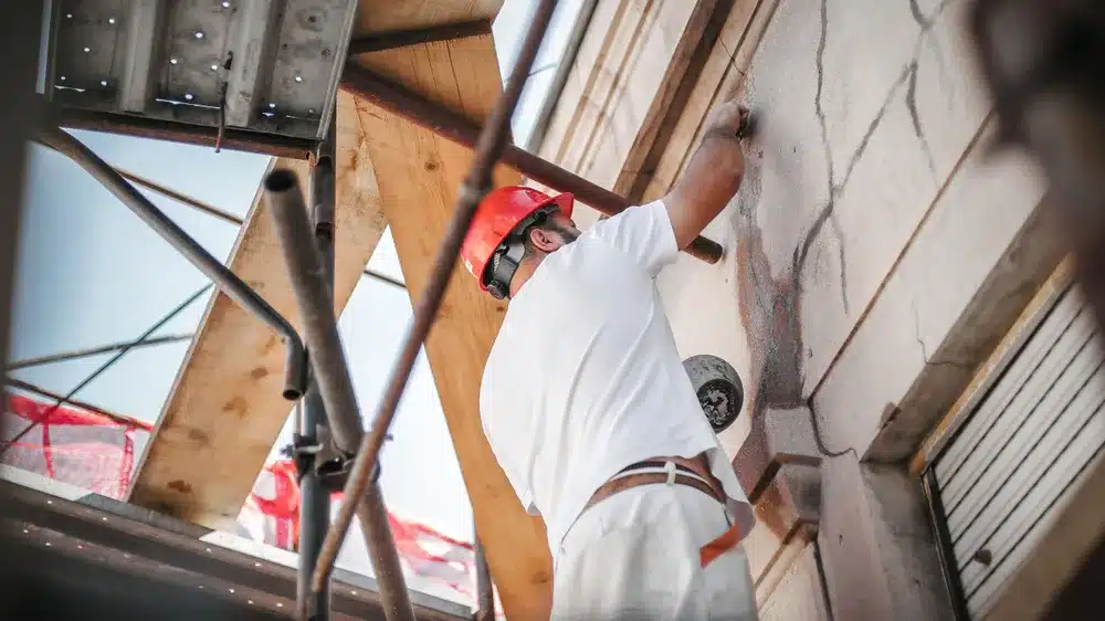 A worker on scaffolding repairing cracks in an exterior building facade — restoration contractor insurance in Colorado