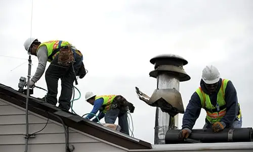 A crew in safety vests repairing roof vents and flashing after storm damage — restoration contractor insurance in Texas
