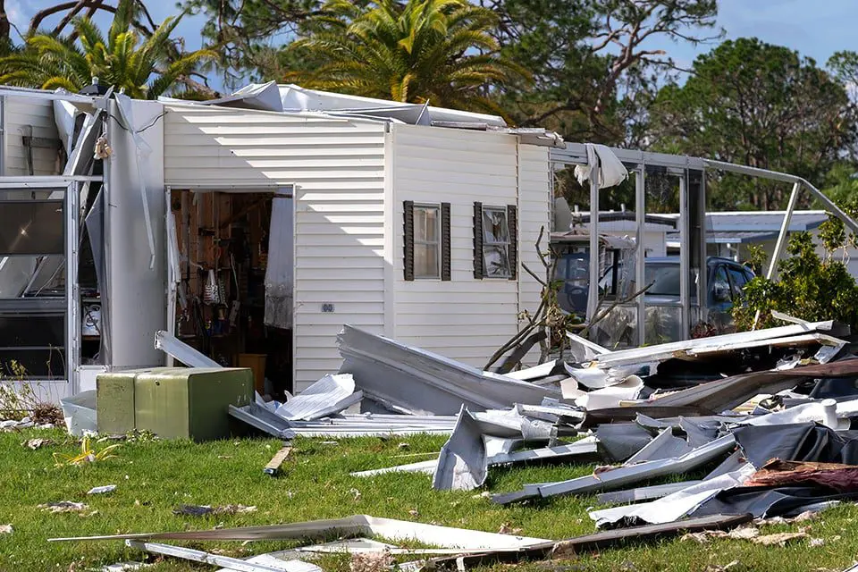 A storm-damaged manufactured home with torn siding and scattered debris across the yard — restoration contractor insurance in Georgia