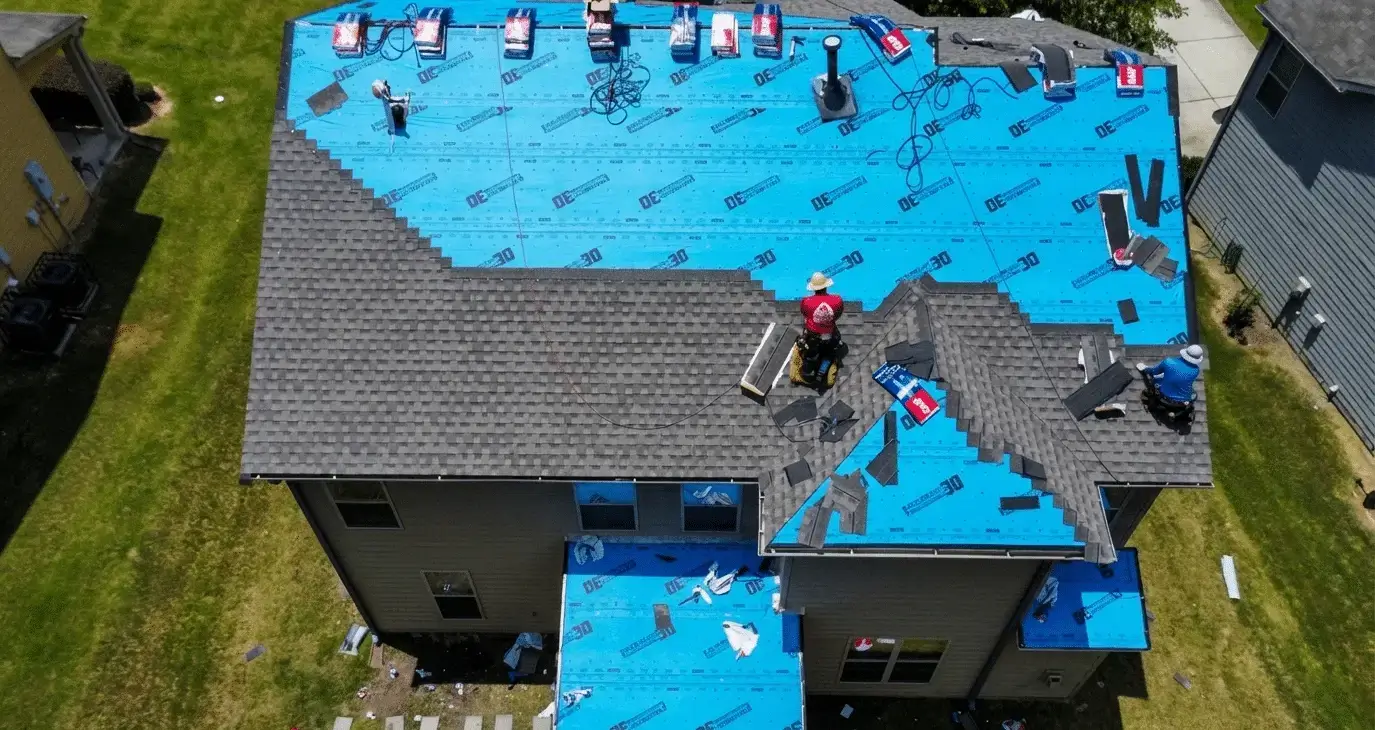 An aerial view of a roofing crew laying synthetic underlayment and shingles on a large house — restoration contractor insurance in California